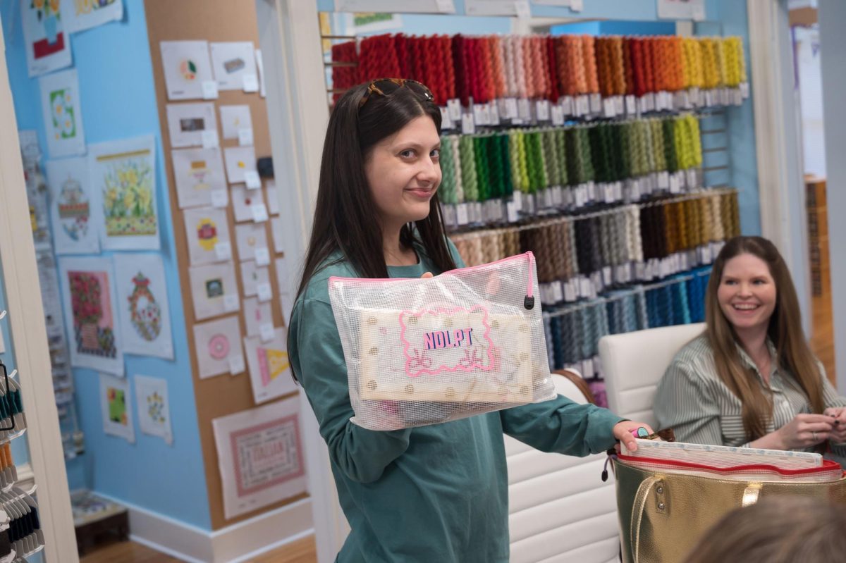 Stitch Social BR member Rebecca Atkins holds up her custom-made needlepoint bag, Monday, March 17, at the Elegant Needle.